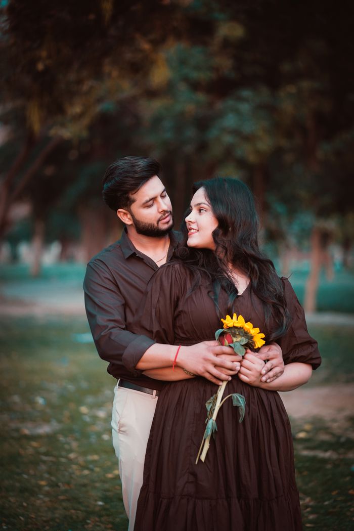A couple enjoying an intimate outdoor photoshoot, holding a sunflower in a serene park.