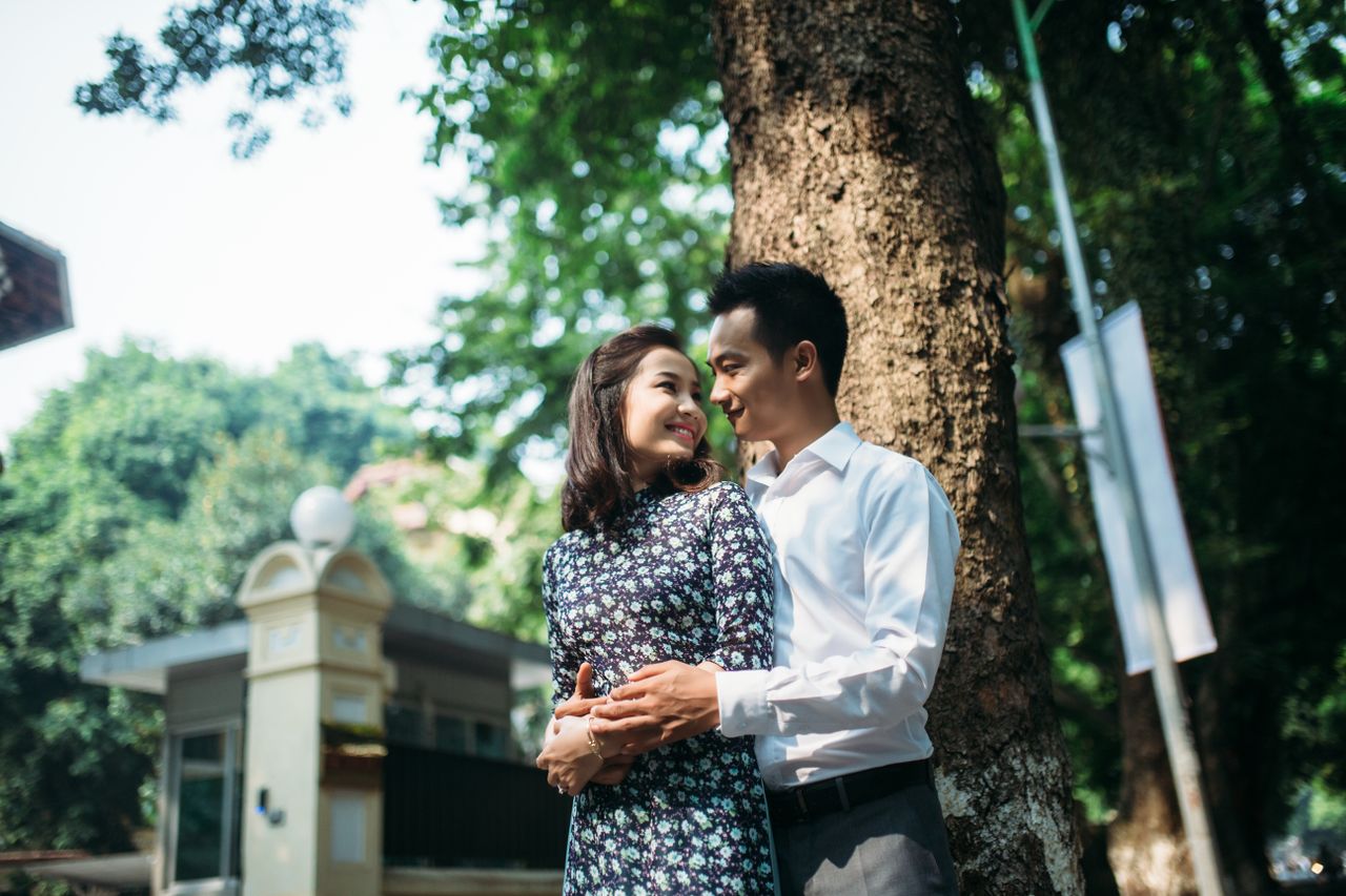 A happy couple embraces under a tree in a sunny park, conveying love and joy.
